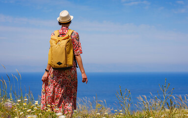 summer trip to Rhodes island, Greece. Young Asian woman in ethnic red dress and yellow backpack...