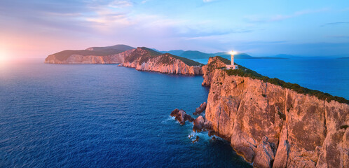 Fototapeta na wymiar Panoramic, aerial view of Cape Ducato cliffs and sea with lighthouse shining, illuminated by pink light of setting sun. Lefkada, Greece.