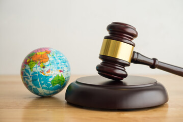 Hammer judge gavel and world globe in courtroom with white wall background. World court, International Court of Justice (ICJ) concept. World court adjudicates general disputes between countries. - obrazy, fototapety, plakaty