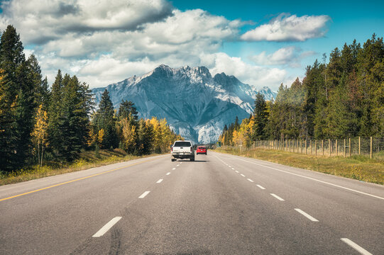 Car driving on highway to rocky mountains in autumn forest at national park