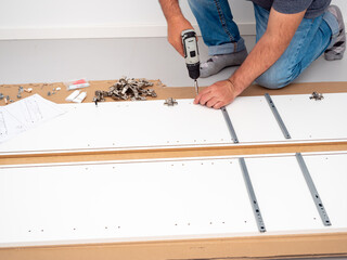 A man assembles furniture at home with a professional screwdriver. Furniture assembly.