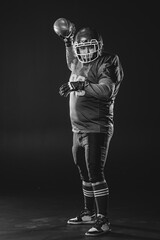 Portrait of a man in uniform for american football throws the ball on a black background. Monochrome. 