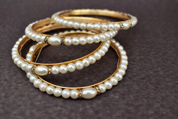 A closeup selective focus picture of a Gold bangles with Pearls .