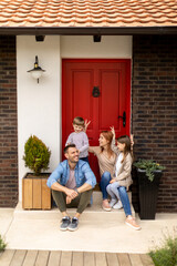 Family with a mother, father, son and daughter sitting outside on the steps of a front porch of a...