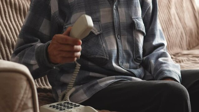 a lonely elderly man sitting at home on the couch takes a corded phone answering a call. a pensioner is talking on a landline home phone