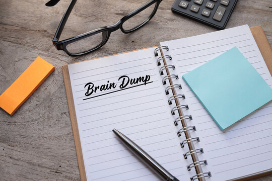 Brain Dump, two words written in black ink on a white paper notebook on the wooden table.  