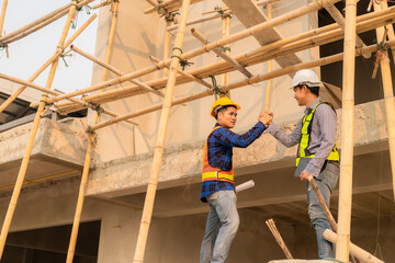 Naklejka na ściany i meble Asian construction architects and engineers shaking hands while working for teamwork and collaboration concept working together house plans on construction site