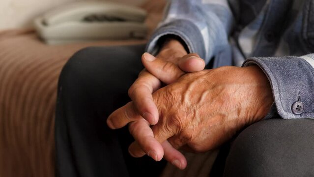 hands of an elderly man pensive at home sitting near a fixed wire telephone waiting for a phone call, news, emotions of old people