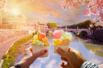 Couple with beautiful bright sweet Italian ice cream with different flavors  in the hands .Saint Angel Castle and bridge over the Tiber river.Traveling concept background in Rome, Italy 
