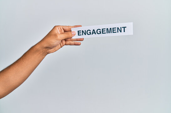 Hand of caucasian man holding paper with engagement word over isolated white background - Powered by Adobe