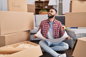 Young hispanic man architect smiling confident reading house plans at new home