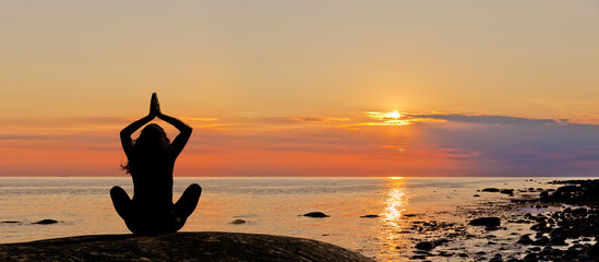 eine Frau zelebriert Yoga bei Sonnenuntergang am Meeresstrand