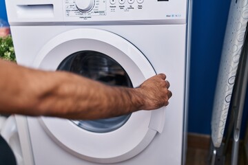 Young hispanic man closing washing machine at laundry room