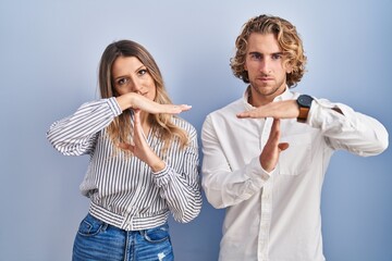 Young couple standing over blue background doing time out gesture with hands, frustrated and...
