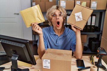 Young man working at small business ecommerce holding packages afraid and shocked with surprise and amazed expression, fear and excited face.