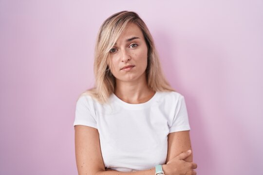 Young blonde woman standing over pink background looking sleepy and tired, exhausted for fatigue and hangover, lazy eyes in the morning.