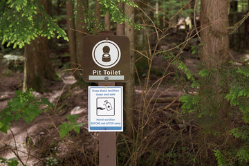 Pit toilet signage and hand-sanitizing sign on fence pole. Information placards about outhouse,...