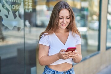 Young blonde woman smiling confident using smartphone at street