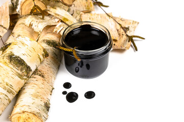 Birch tar or pitch in a jar and birch tree bark on white background. Wood tar. Liquid mineral tar from birch bark