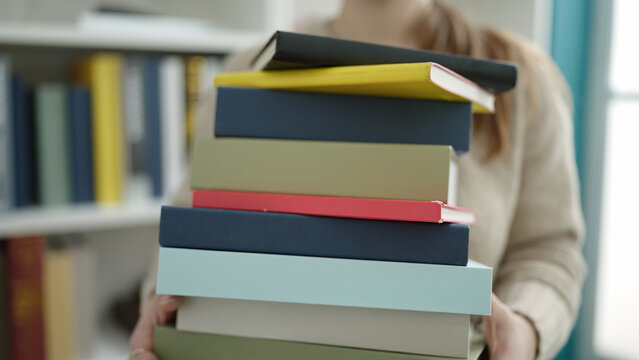 Young blonde woman student holding books at library university