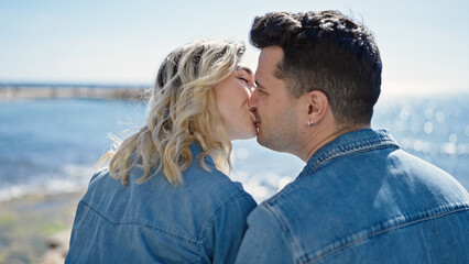 Man and woman couple sitting on bench backwards kissing at seaside