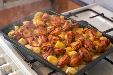 Freshly roasted steaming potatoes with chicken wings in metal baking pan