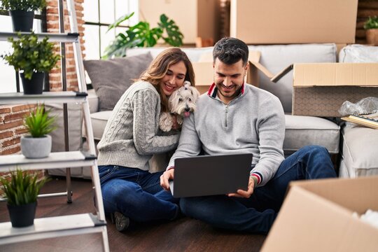 Man and woman using laptop sitting on floor with dog at new home