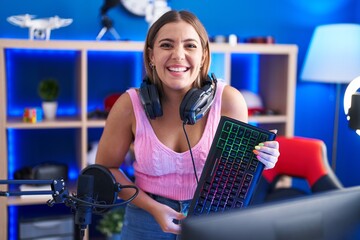 Young blonde woman playing video games holding keyboard smiling and laughing hard out loud because funny crazy joke.