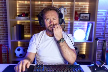 Middle age man with beard playing video games wearing headphones looking stressed and nervous with...