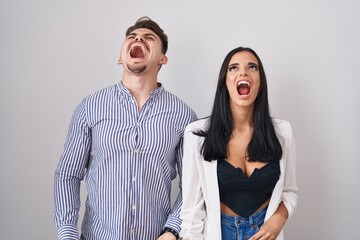 Young hispanic couple standing over white background angry and mad screaming frustrated and furious, shouting with anger. rage and aggressive concept.
