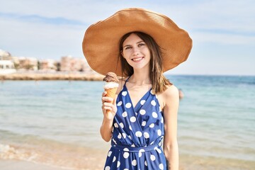 Fototapeta na wymiar Young blonde woman tourist wearing summer hat holding ice cream at beach