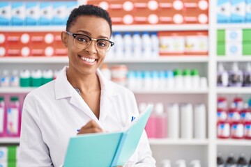 Obraz na płótnie Canvas African american woman pharmacist writing on document at pharmacy