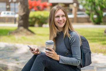 Young blonde woman at outdoors using mobile phone and holding a take away coffee