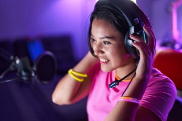 Young hispanic woman streamer smiling confident sitting on table at gaming room