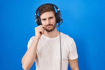 Hispanic man with beard listening to music wearing headphones mouth and lips shut as zip with fingers. secret and silent, taboo talking