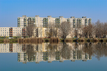 Fototapeta na wymiar Colorful panel houses standing on the shore of a lake, reflected in the water. Housing estate in Hungary.