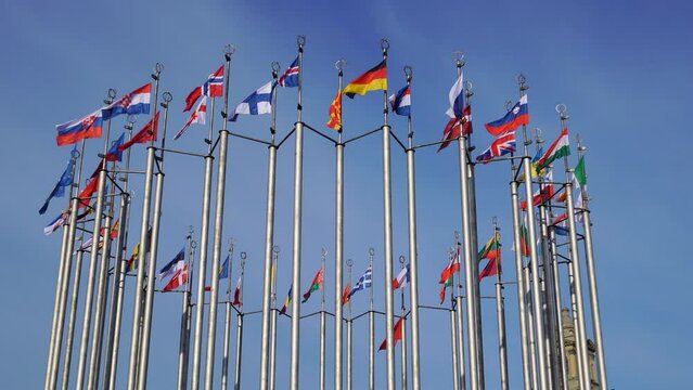 Many European country flags waving on flagpoles on windy day on blue sky background.