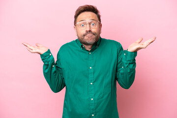 Middle age caucasian man isolated on pink background having doubts while raising hands