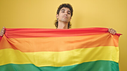 Young hispanic man holding rainbow flag with relaxed expression over isolated yellow background