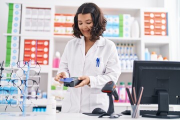 Young woman pharmacist holding using credit card and data phone at pharmacy