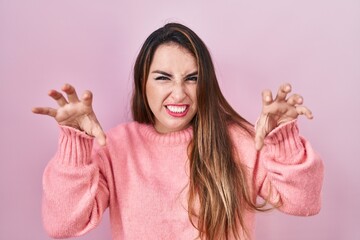 Young hispanic woman standing over pink background smiling funny doing claw gesture as cat,...