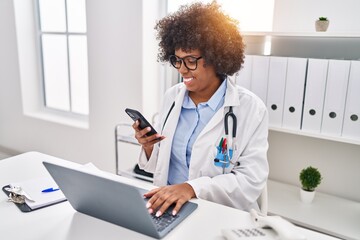 African american woman doctor using smartphone and laptop working at clinic