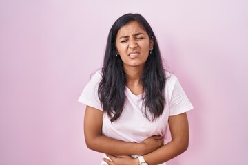 Young hispanic woman standing over pink background with hand on stomach because indigestion, painful illness feeling unwell. ache concept.