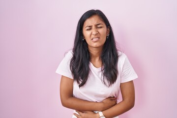 Fototapeta premium Young hispanic woman standing over pink background with hand on stomach because indigestion, painful illness feeling unwell. ache concept.