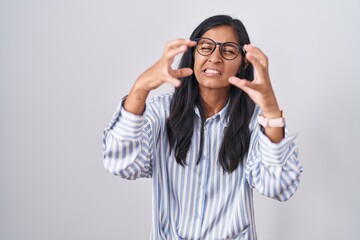 Young hispanic woman wearing glasses shouting frustrated with rage, hands trying to strangle, yelling mad