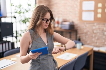 Caucasian woman working at the office wearing glasses checking the time on wrist watch, relaxed and...