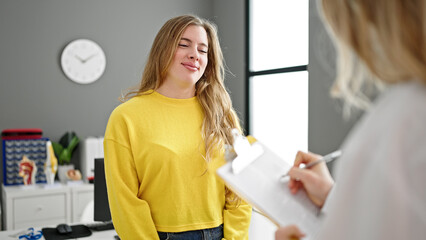 Fototapeta premium Young blonde woman doctor and patient having medical consultation writing medical report at clinic