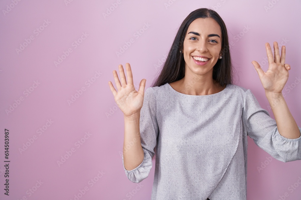 Wall mural Young brunette woman standing over pink background showing and pointing up with fingers number nine while smiling confident and happy.