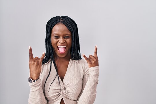 African woman with braids standing over white background shouting with crazy expression doing rock symbol with hands up. music star. heavy music concept.