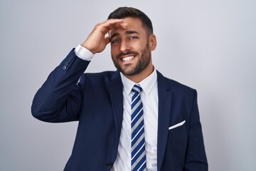 Handsome hispanic man wearing suit and tie smiling confident touching hair with hand up gesture, posing attractive and fashionable